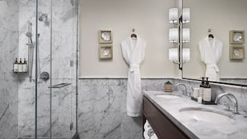 Un baño moderno con cabina de ducha de vidrio, paredes de mármol, un espejo grande y tocador con lavabo y perchero para toallas.