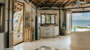 A room with a thatched roof, a large window with a view of the ocean, a kitchenette, and a patterned rug. - Casa Gaia ~ Mahayana, Private Vacation Home on Tulum beach with turquoise sea at your doorstep! (Tulum)