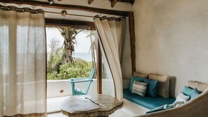 A cozy room with a sofa and a table, a view of the ocean, and a balcony with a chair. - Casa Gaia ~ Mahayana, Private Vacation Home on Tulum beach with turquoise sea at your doorstep! (Tulum)