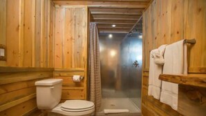 A wooden bathroom with a toilet, shower, and wooden walls.