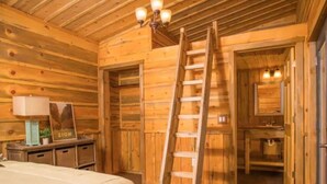 A wooden cabin interior with a bed, a ladder, a desk, and a kitchenette.