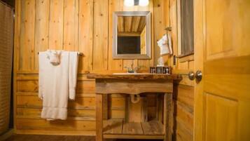 Ein Badezimmer einer Holzhütte mit Waschbecken, Spiegel, Handtuchhalter und einer hölzernen Bank.