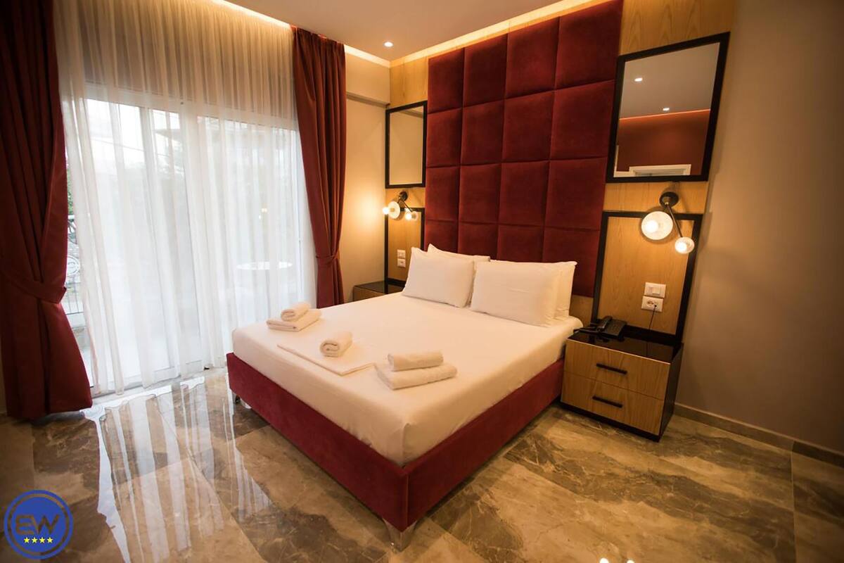 A hotel room with a large bed, a bedside table with a lamp, a mirror, and a window with curtains.