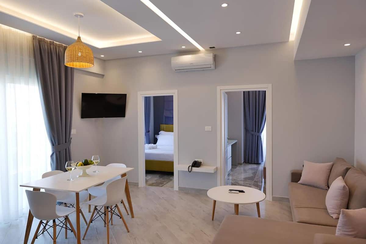 A modern hotel room with a dining area, a sofa, a TV, and a bed.