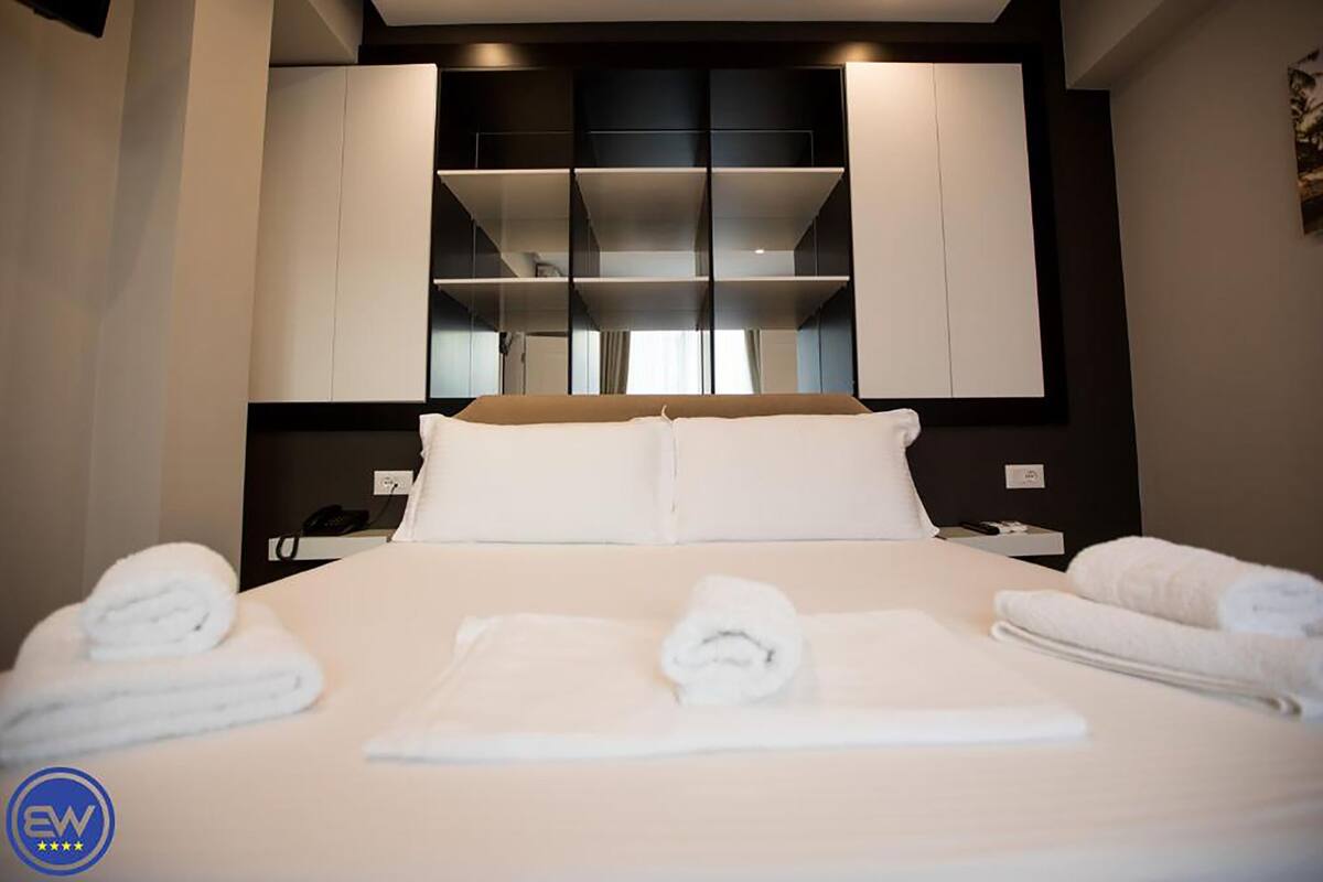 A hotel room with a large bed, white linens, a bedside table with a phone, and built-in cabinets above the bed.