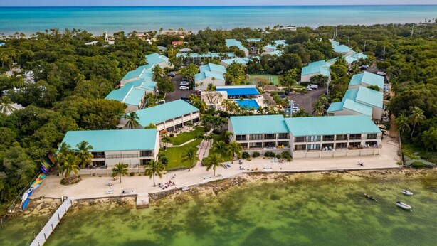An aerial view of a resort with multiple buildings, a beach, and clear turquoise waters.