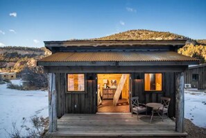 Una cabaña rústica con fachada de madera, un porche con mesa y sillas, y vistas a un paisaje montañoso.