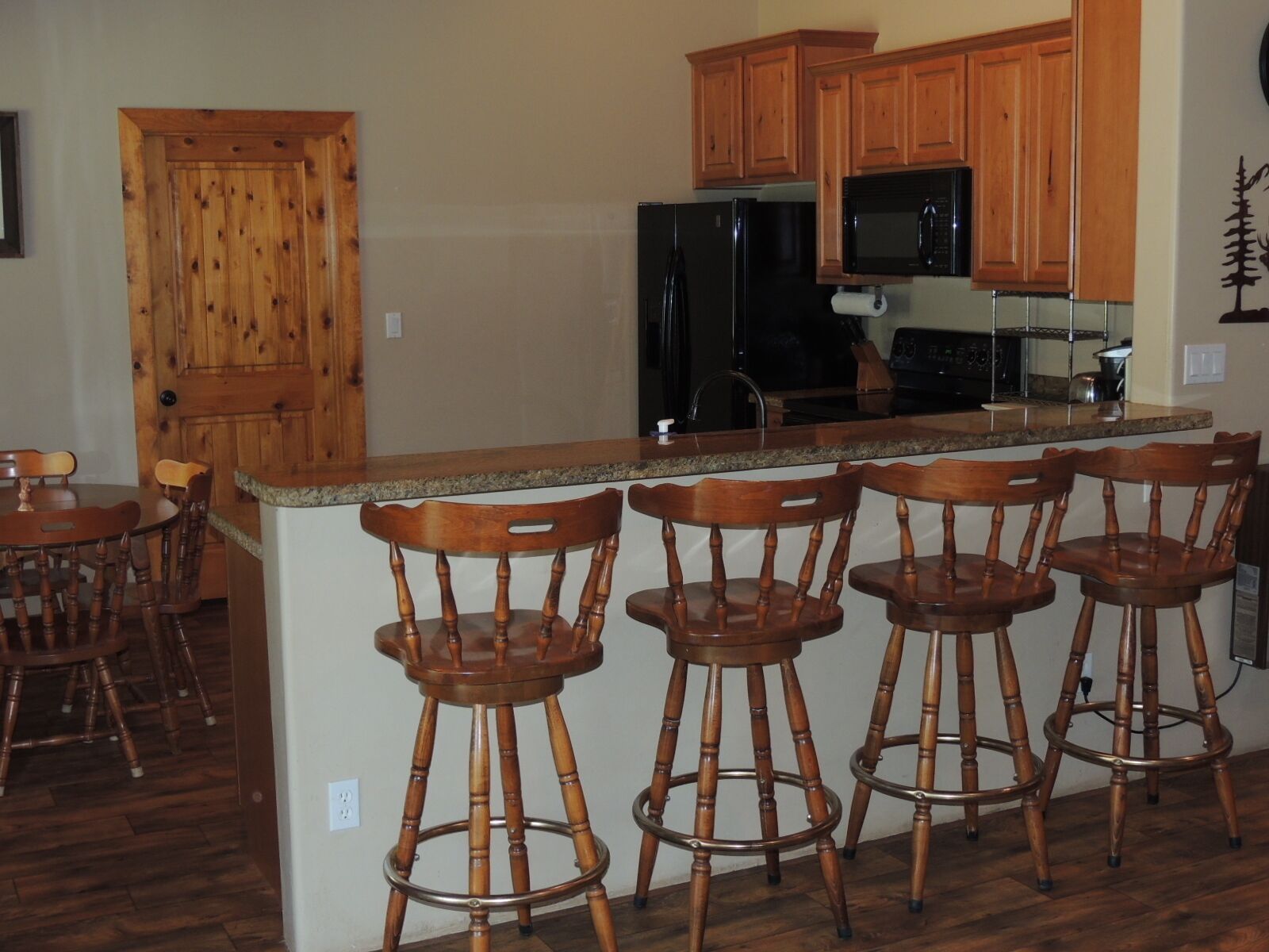 A kitchen with wooden cabinets, a black refrigerator, a microwave, and a bar stool area.