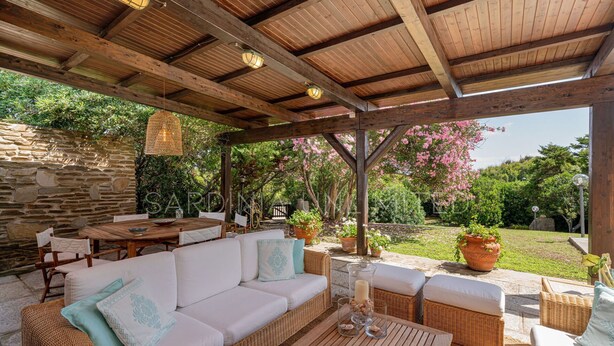 En udendørs terrasse med et træpergola, fletmøbler og plantekasser.