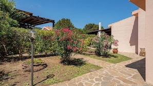 En have med stenhinner, blomstrende planter og en pergola.