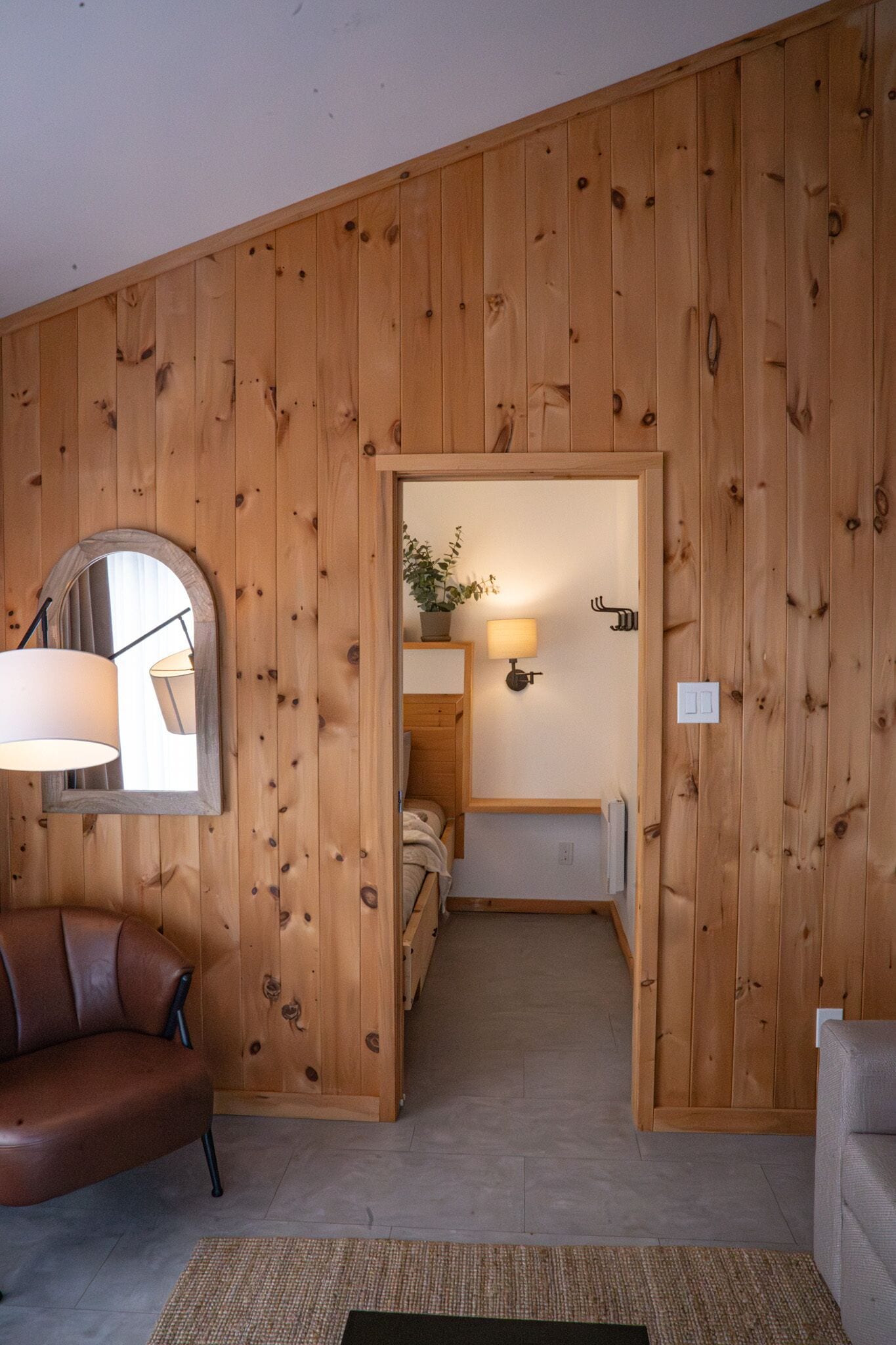 A room with wooden panel walls, a brown leather chair, a small table with a lamp, and a bed with a nightstand.