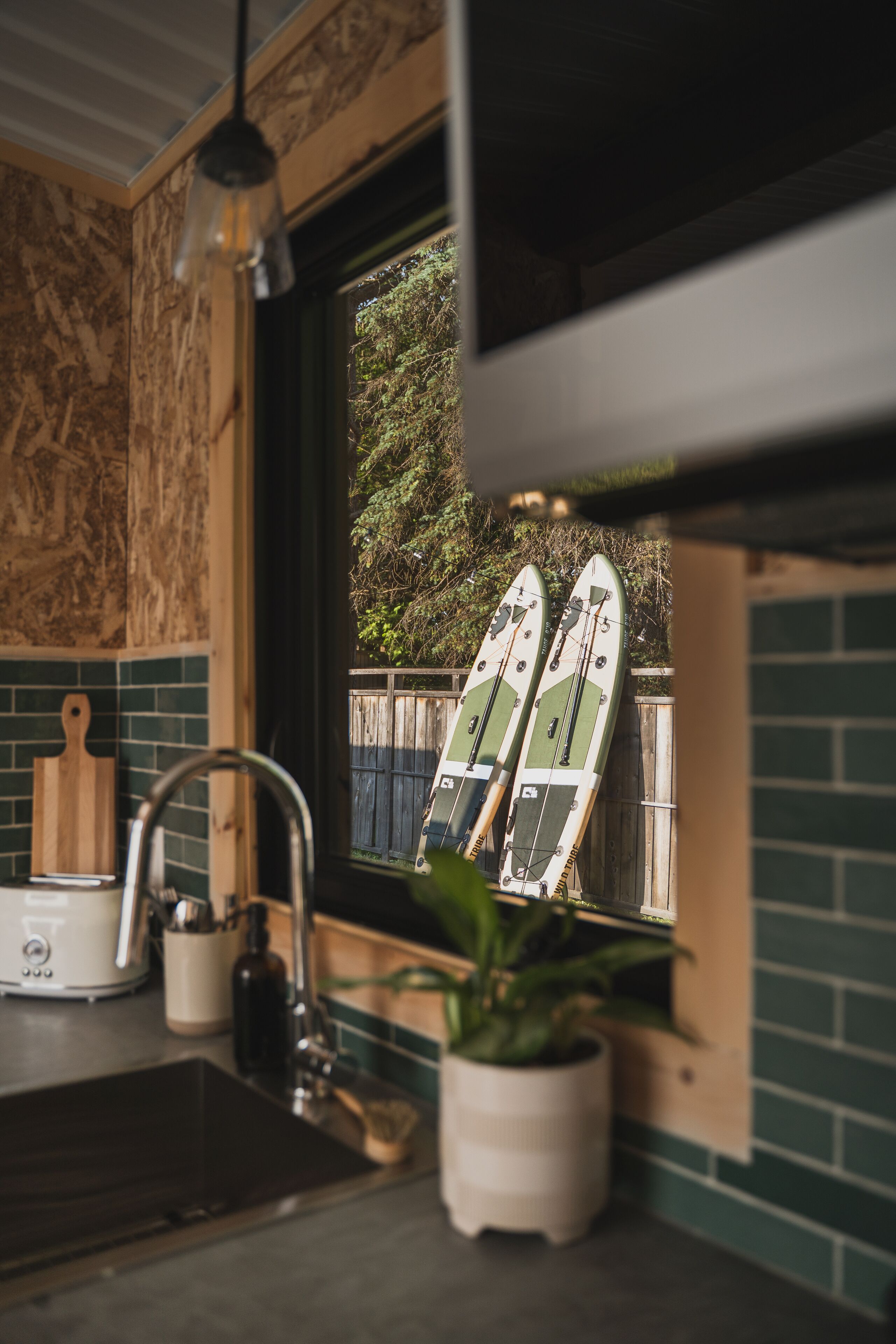 Une cuisine avec une fenêtre, une plante et deux planches de surf appuyées contre le mur.