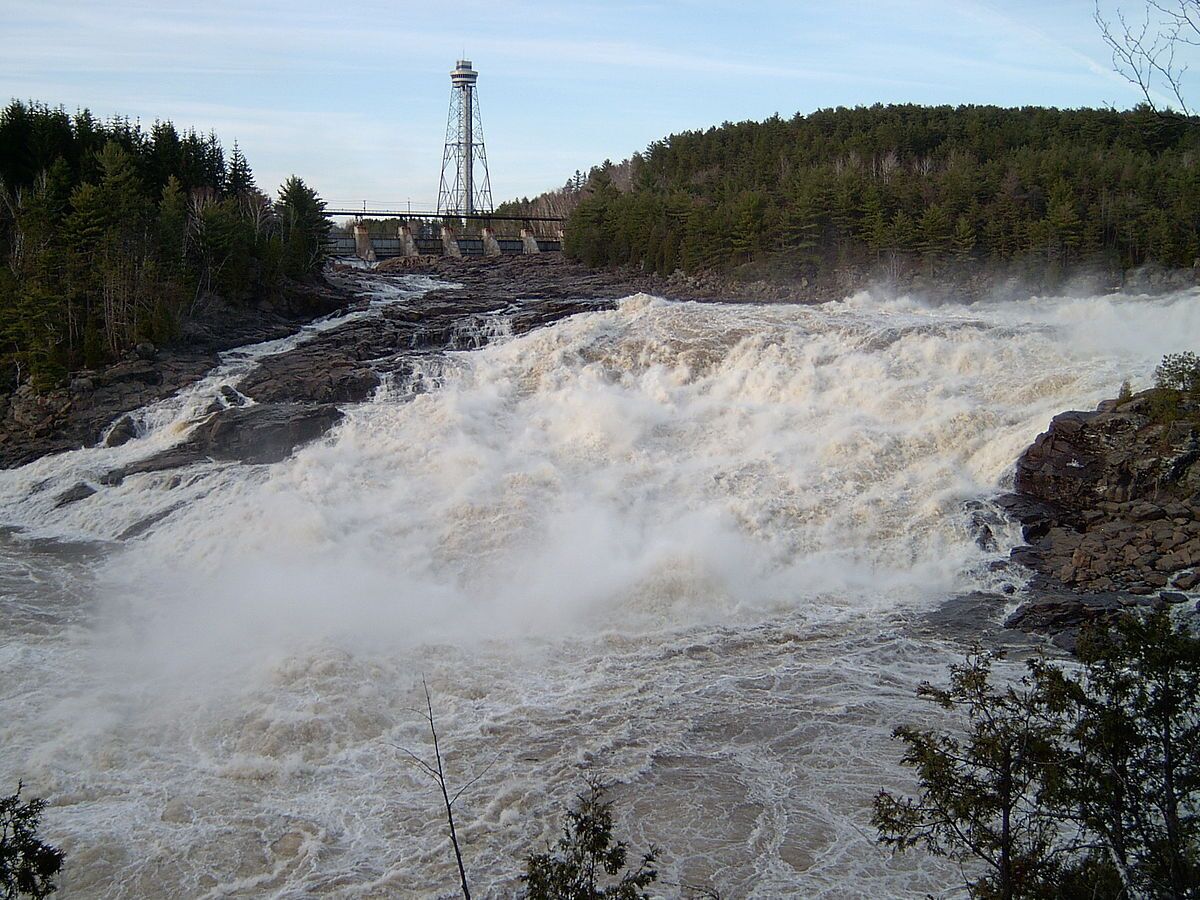 A large waterfall with a dam and a tower in the background.
