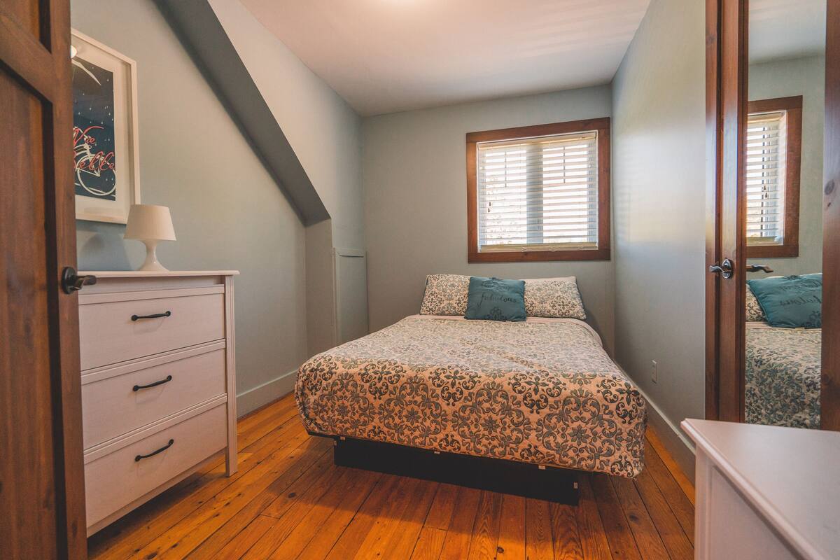 Quarto com cama, penteadeira, janela e porta.