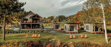 Un complexe hôtelier moderne de style chalet, doté d’un grand bâtiment principal et de plusieurs petits chalets, entouré d’une zone verdoyante avec des espaces de détente en plein air et offrant une vue panoramique sur les arbres et les collines.