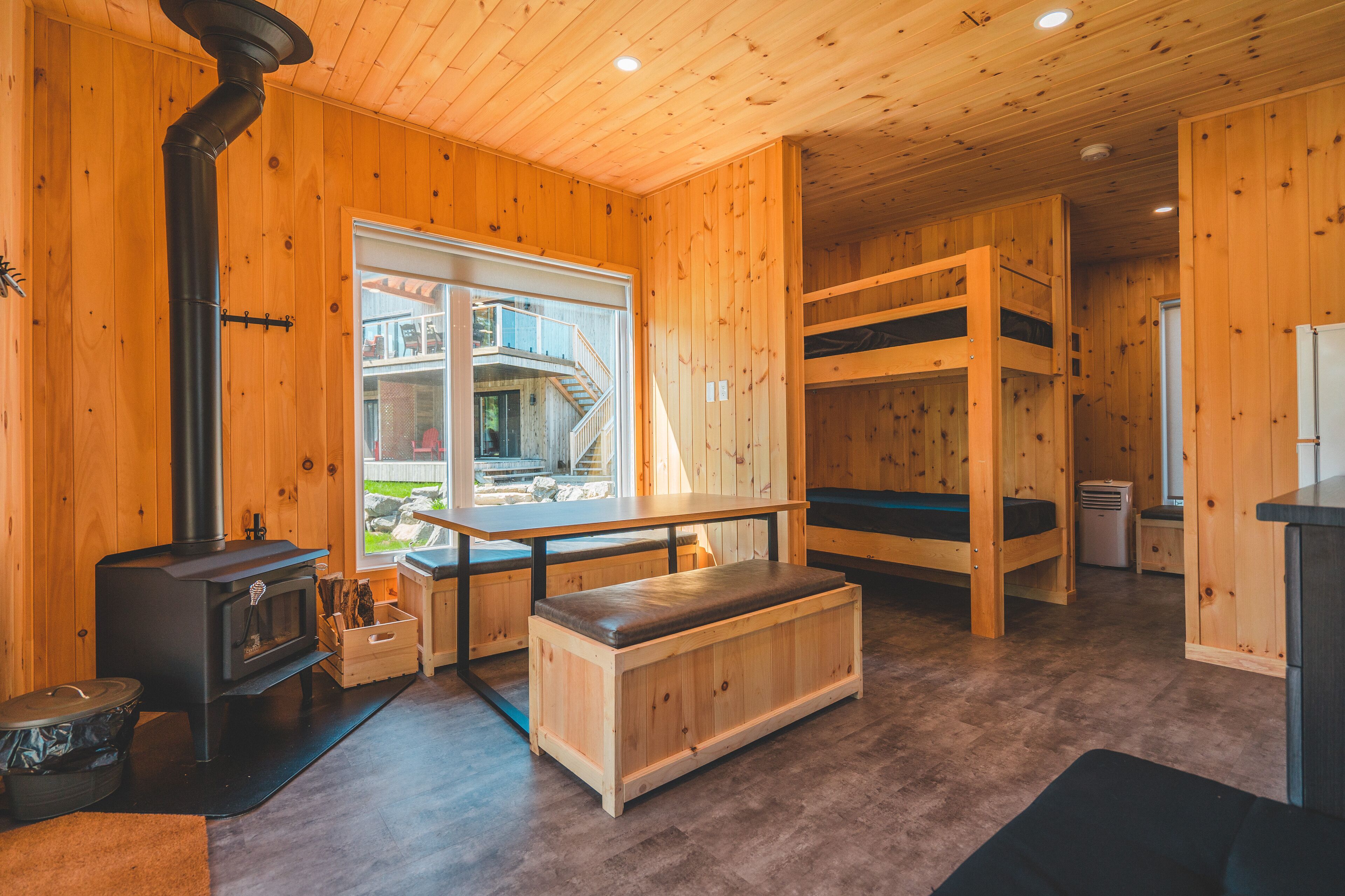 A cabin with a wood-burning stove, bunk beds, a dining area, and a view of a mountain.