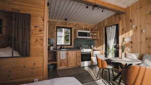 A cozy cabin-style room with a bed, a dining table with chairs, a kitchen area with a microwave, stove, and cabinets. - Le 2800 du Parc (Shawinigan)