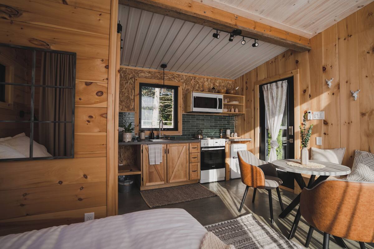 Um quarto acolhedor em estilo cabana, com cama, mesa de jantar e cadeiras, cozinha equipada com micro-ondas, fogão e armários.