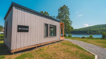 Une cabane en bois avec une enseigne indiquant « Le Cadorette », un chemin de gravier et un lac en arrière-plan.