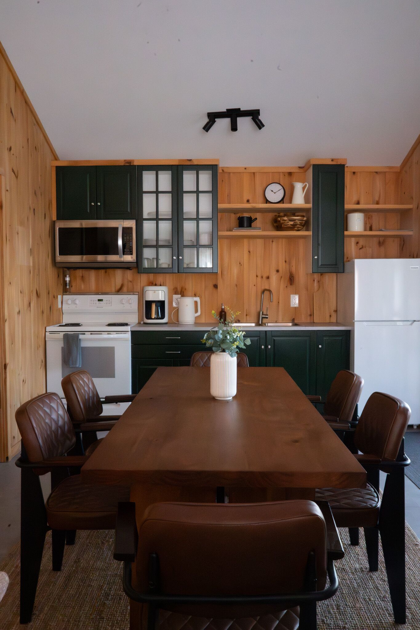 Une cuisine dotée de meubles en bois, d’un four à micro-ondes, d’une cuisinière, d’une machine à café et d’une table  à manger avec des chaises.