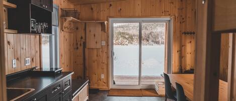 A wooden interior with a kitchen area, a dining table, and a sliding glass door leading to a snowy outdoor area.