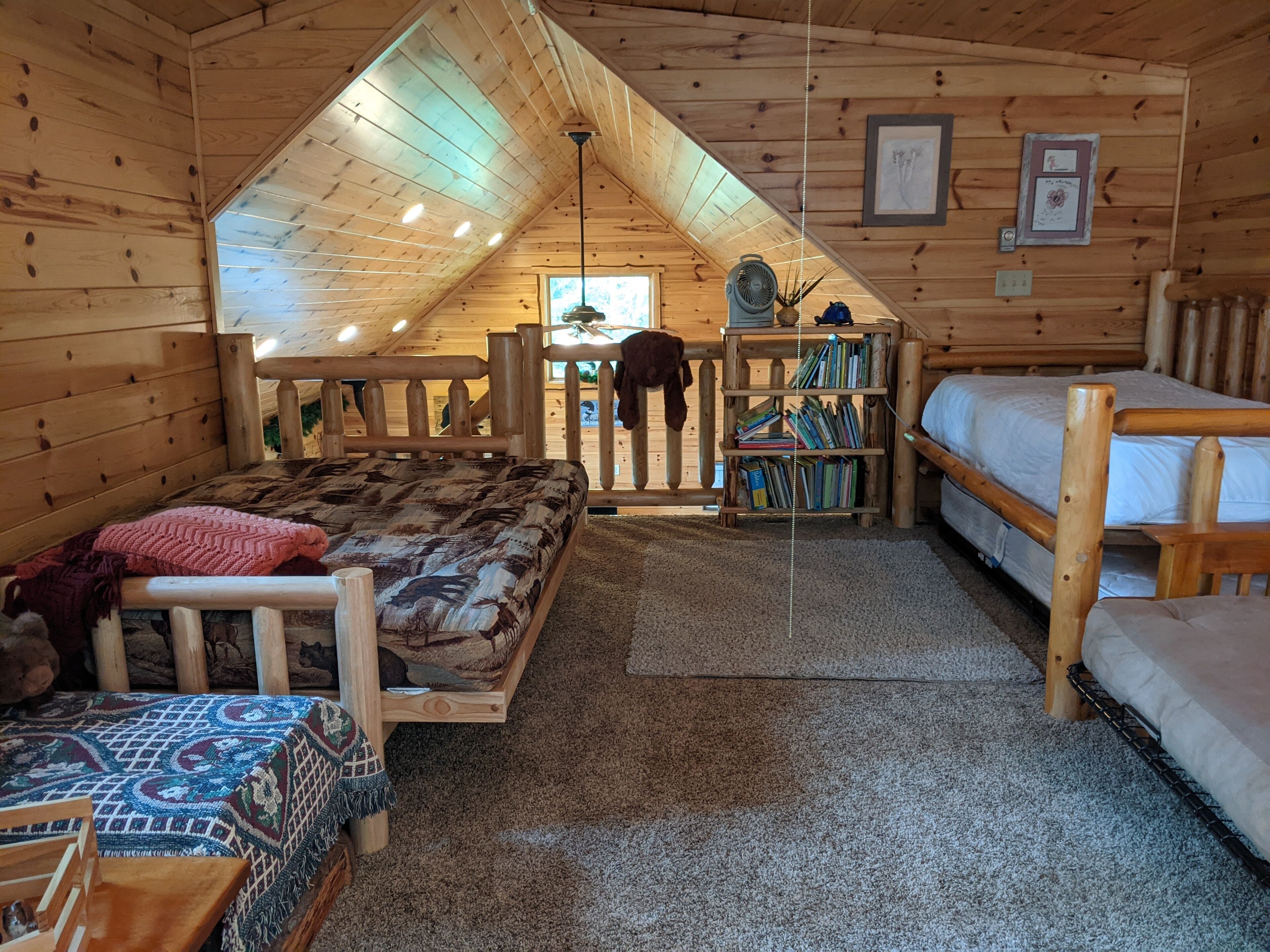 Ein gemütliches Schlafzimmer im Dachgeschoss mit schrägem Giebeldach, Holzwänden, einem Etagenbett, einem kleinen Schreibtisch und einem Bücherregal.