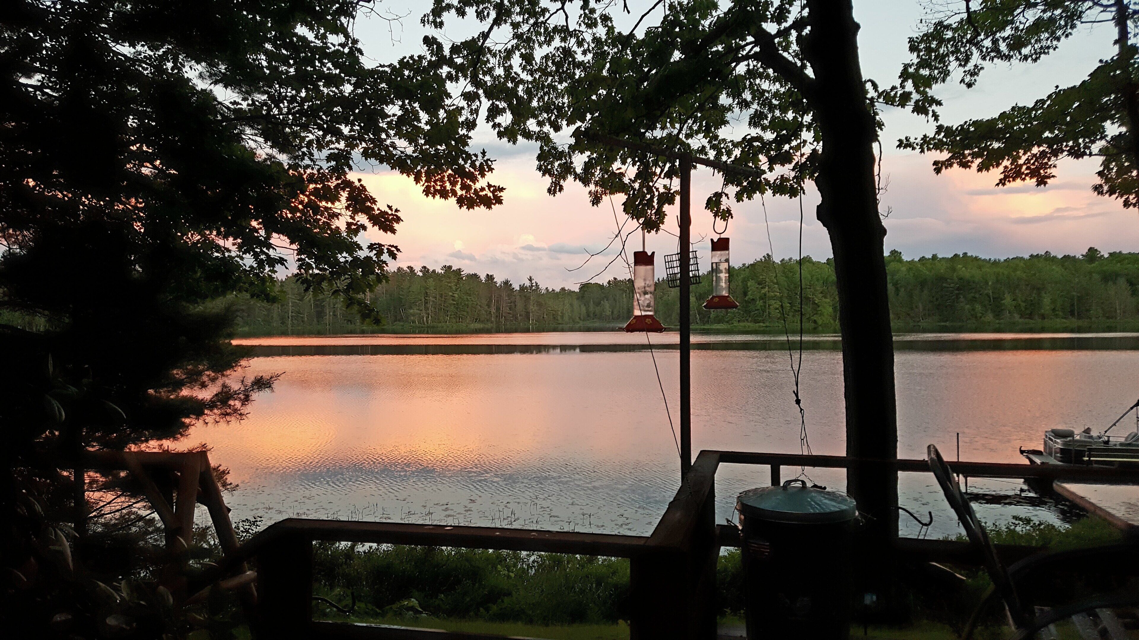 A lakeside view with a dock, a fishing boat, and a red and white buoy in the distance.