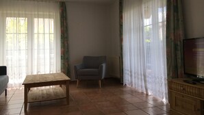 Una sala de estar con una mesa de madera, un sillón gris, un televisor sobre un mueble de madera y un radiador.