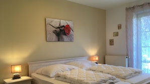 Un dormitorio con cama, mesitas de noche, lámpara, radiador y ventana con cortinas.