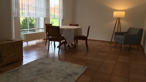 Un comedor con una mesa redonda, sillas, una lámpara y vistas al exterior con vegetación.