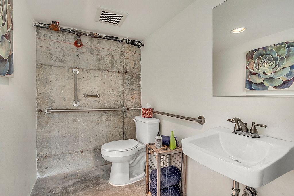 A bathroom with a concrete shower wall, a white toilet, a sink, and a towel rack.