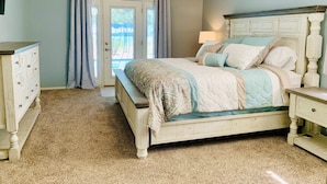 A bedroom with a bed, a dresser, a nightstand, a ceiling fan, and a wall with a decorative phrase. - Wildflower Ranch Backyard Oasis with Pool & Spa (Goodyear)