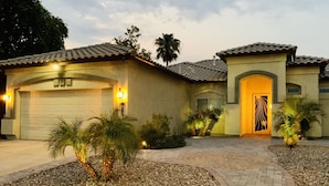 A residential house with a garage, a driveway, and landscaped areas with palm trees. - Wildflower Ranch Backyard Oasis with Pool & Spa (Goodyear)