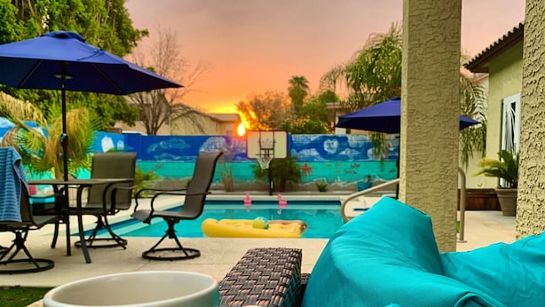 A poolside seating area with a white mug, a blue sofa, and a wicker chair. - Wildflower Ranch Backyard Oasis with Pool & Spa (Goodyear)