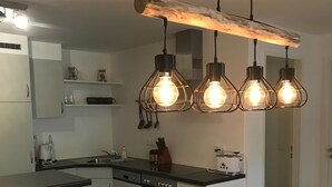 Eine moderne Küche mit weißen Schränken, einer schwarzen Arbeitsplatte und einer Deckenleuchte mit Holzbalken.