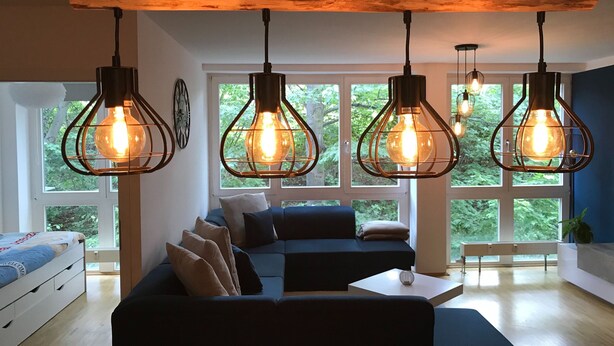 Ein modernes Wohnzimmer mit einem Ecksofa, einem Couchtisch und drei hängenden Pendelleuchten mit freiliegenden Glühbirnen.
