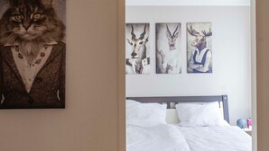 Ein Schlafzimmer mit einem Bett, Holzboden und Wandbildern, darunter Katzen- und Hirschgemälde.