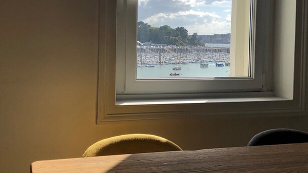 Une vue depuis une fenêtre donnant sur une marina, avec des bateaux et une côte lointaine.