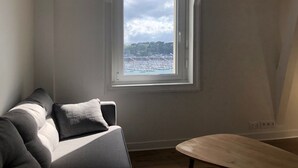 Une pièce avec vue sur un port de plaisance et sur des collines, un canapé gris et un banc en bois.