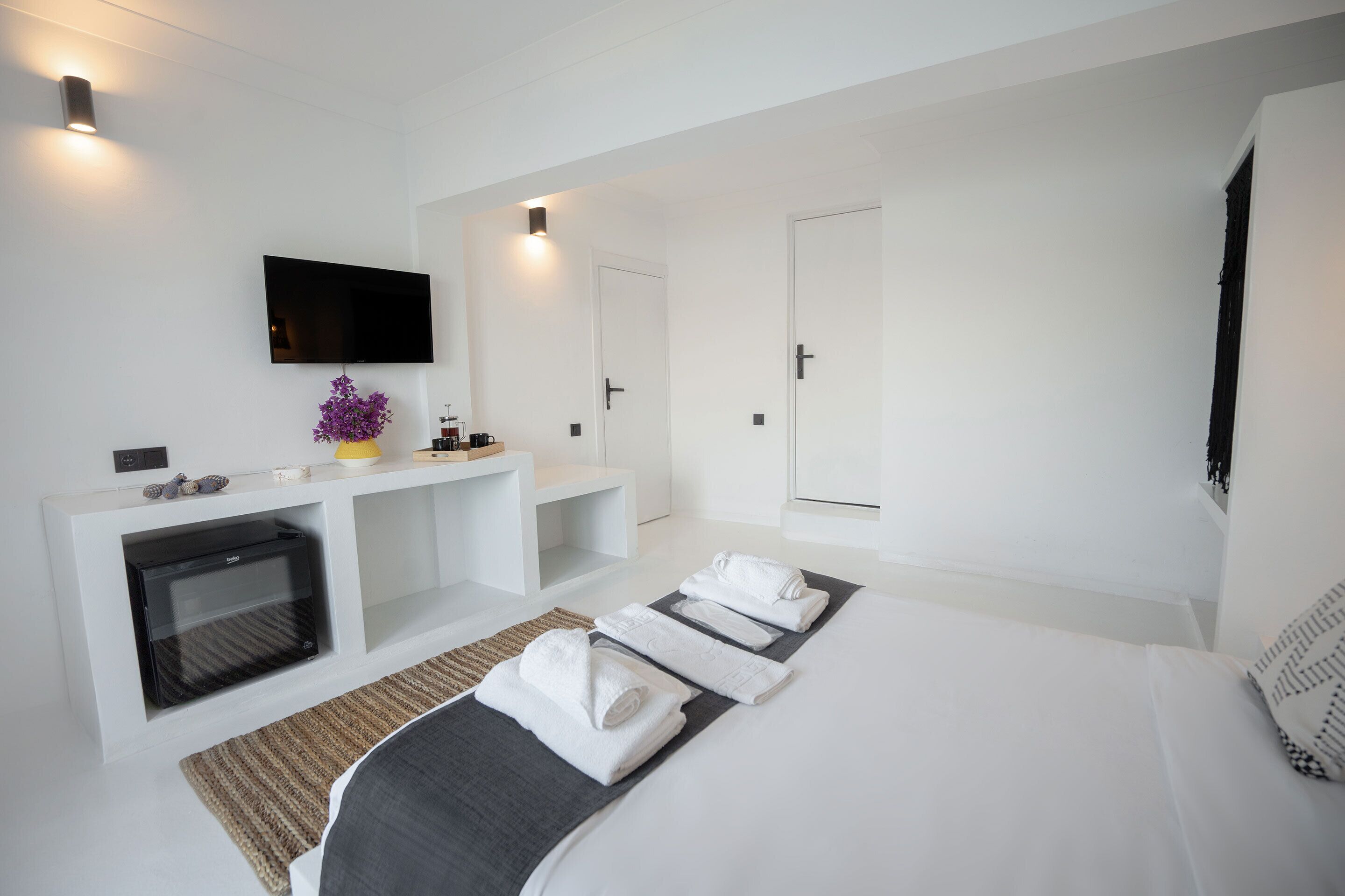 Ein modernes Hotelzimmer mit Wand-Fernseher, integriertem Kamin, einem Bett mit ordentlich gefalteten Handtüchern und einer kleinen Sitzecke mit einer Kaffeemaschine.