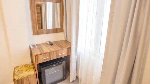 A compact room with a wooden desk, a small refrigerator, a mirror, and a window with curtains. - Camlik 87 Hotel Ayvalik (Ayvalik)