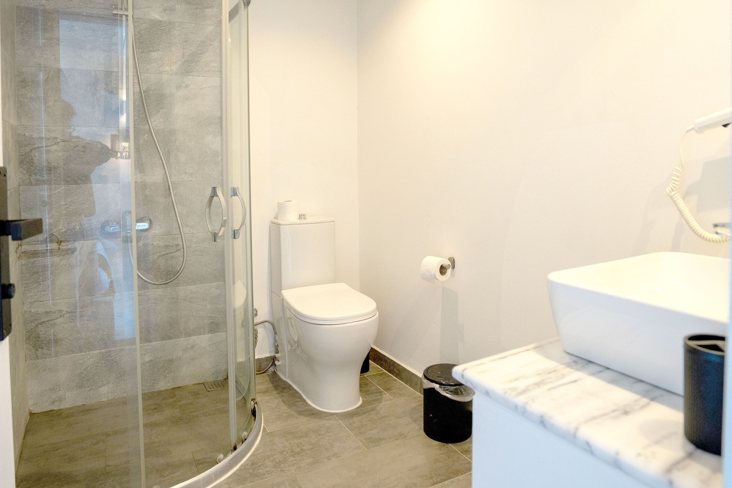 Un baño moderno con ducha envuelta en vidrio, inodoro blanco y encimera de mármol.