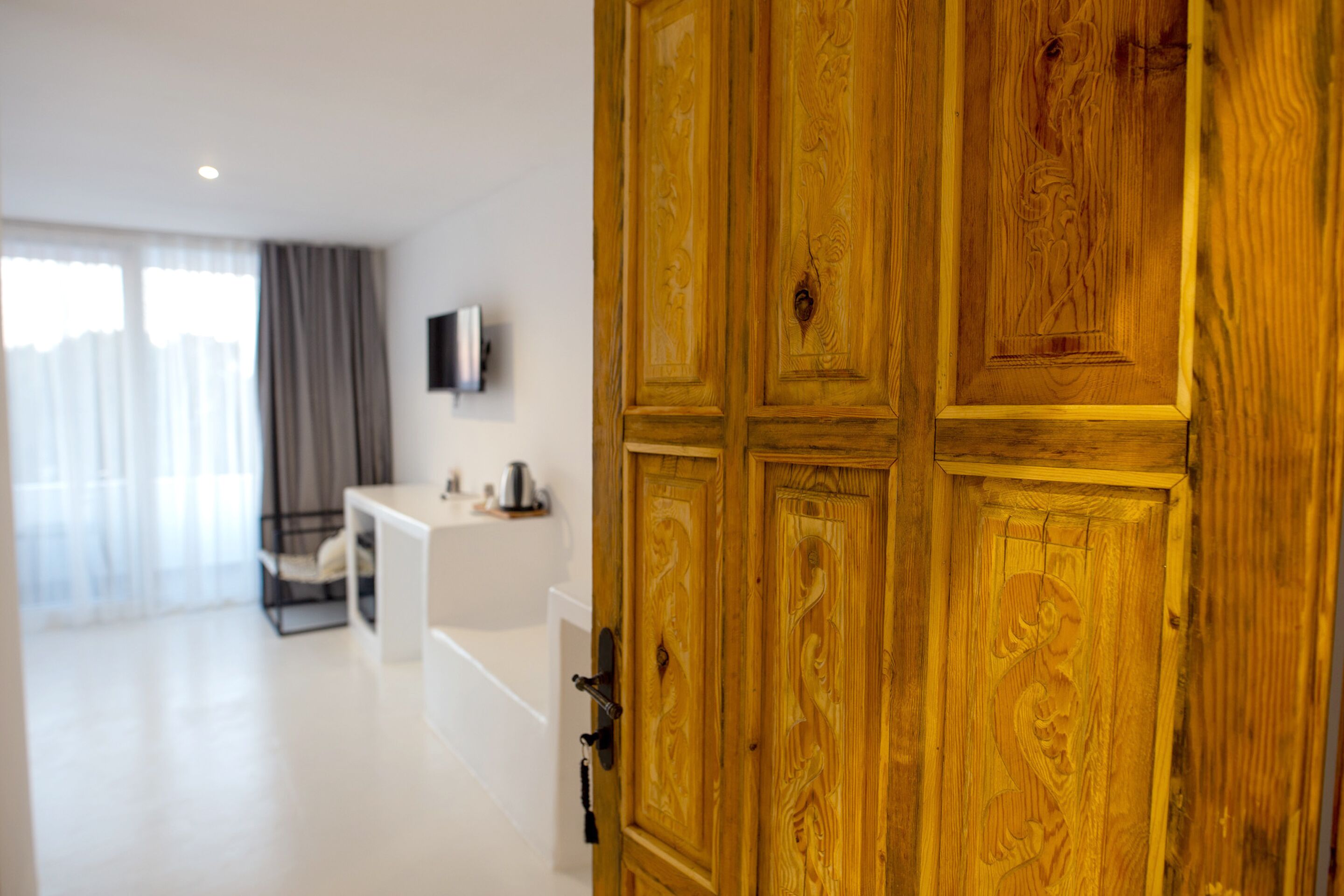 A wooden door with intricate carvings, a white desk, and a television mounted on the wall.
