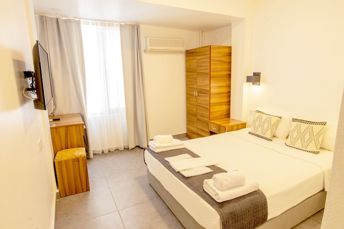 Une chambre d’hôtel avec un lit, une armoire en bois, une télévision et une fenêtre avec des rideaux.