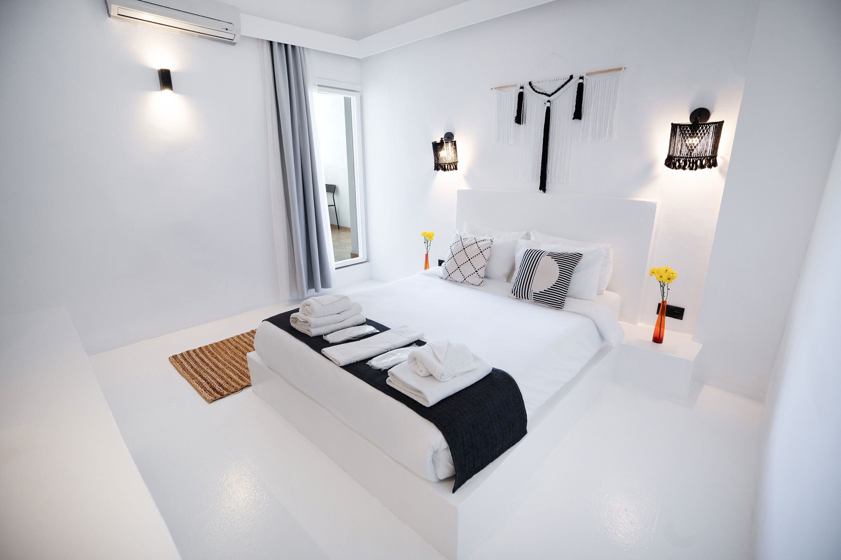 A modern bedroom with a large bed, white walls, and decorative wall sconces.