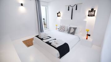 Quarto moderno com uma cama grande, paredes brancas e arandelas decorativas.