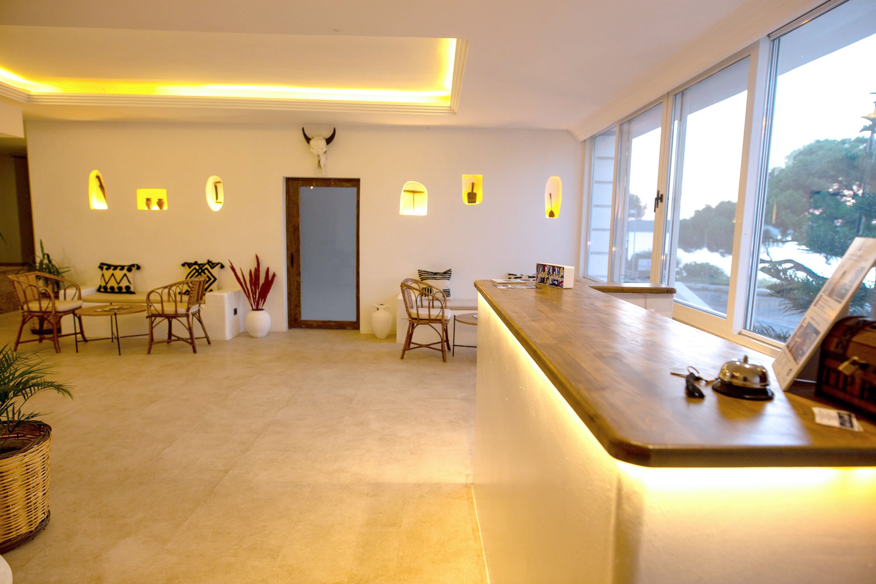 En moderne hotellobby med reception, siddeområde og store vinduer med udsigt udendørs.