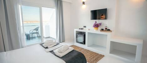 Une chambre d’hôtel moderne avec un grand lit, un téléviseur fixé au mur, un petit bureau agrémenté d’un vase de fleurs et une vue sur la mer par la fenêtre.