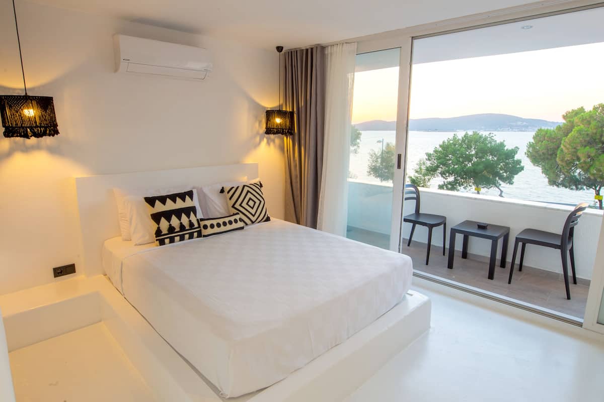 Une chambre d’hôtel moderne dotée d’un grand lit, d’un balcon avec vue sur la mer et d’un coin repas avec tables et chaises.