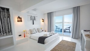Habitación de hotel moderna con una cama grande, vista al mar y un balcón con sillas.